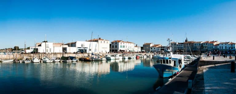 Port animé avec bateaux, ciel bleu et immeubles blancs.