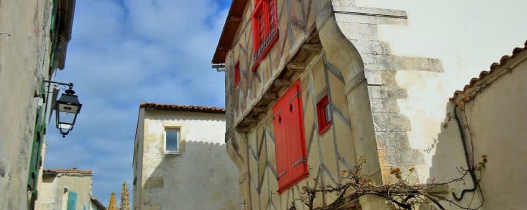 Maison ancienne avec volets rouges, ciel bleu.